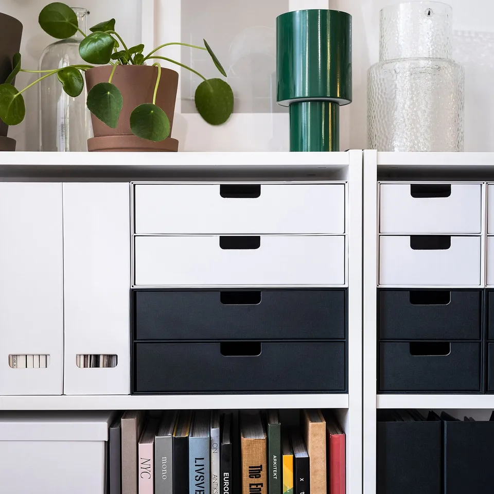 White FJÄDERHARV magazine files on shelf, holding books and papers. Decorative with green lamp and plant.