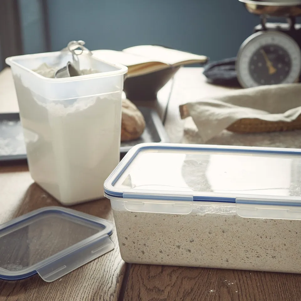 Clear plastic food container with a snap lid sits on a wooden table alongside a container with flour.