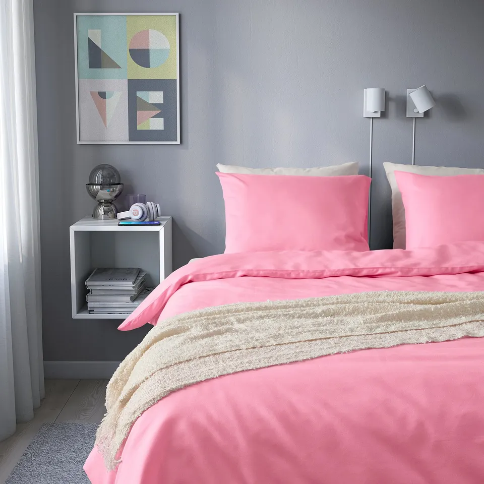 Cosy bed with bright pink PILTANDVINGE duvet, fluffy cover, light wood frame; grey walls.