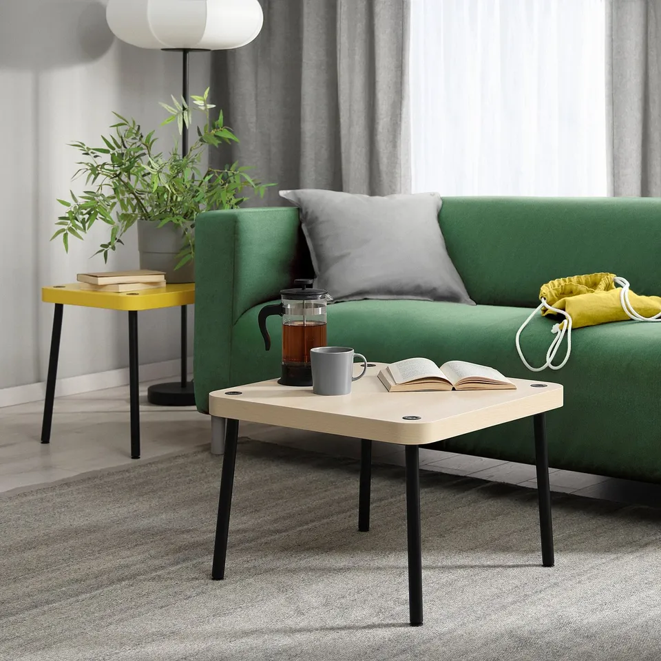 Small SONHULT side table in white and black, modern minimalist design, holding a coffee maker, mug, and book beside a green sofa.