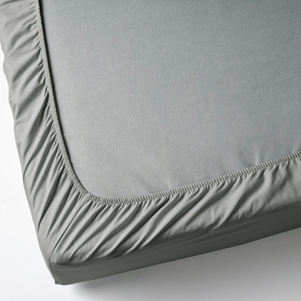 Grey fitted sheet with elastic edges for a secure fit on mattresses up to 26 cm thick, made from soft, breathable cotton.
