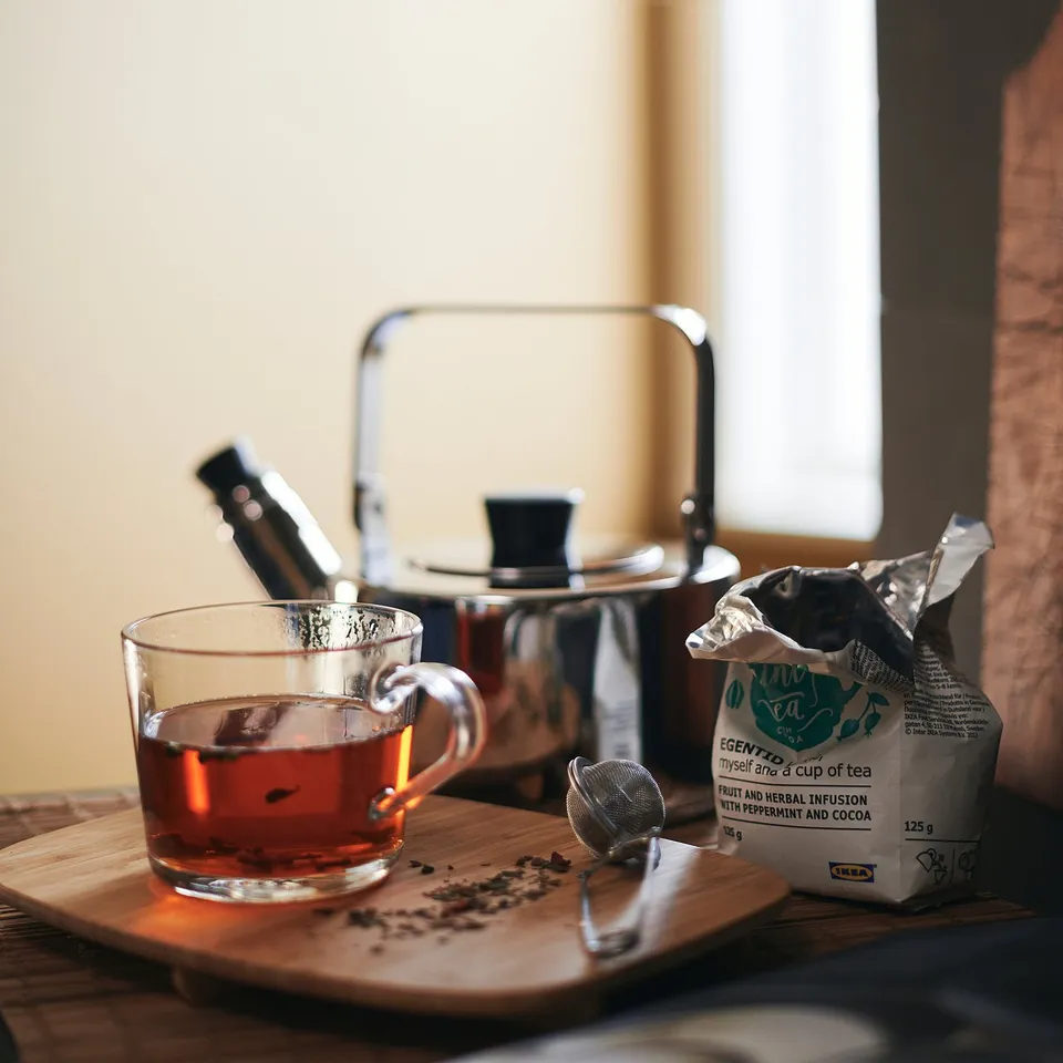 Glass teapot, cup, and tea bag on wooden tray. Enjoy teas aroma and temperature resilience.