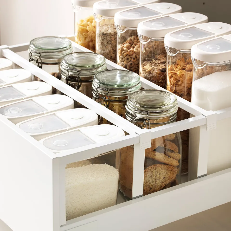 Well-organized pantry drawer with glass jars and clear containers storing various foods, showcasing an efficient kitchen storage system.