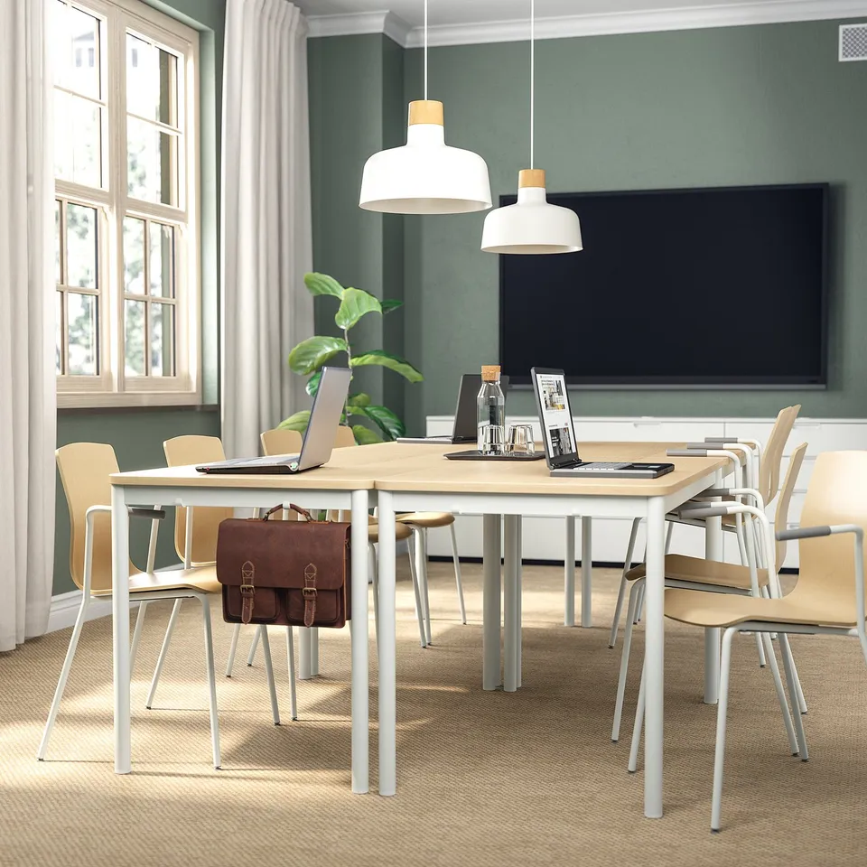 Modern office with wooden LÄKTARE conference table, birch chairs, laptop, files, plant, pendant lamps, green walls, tv, and window with curtains.