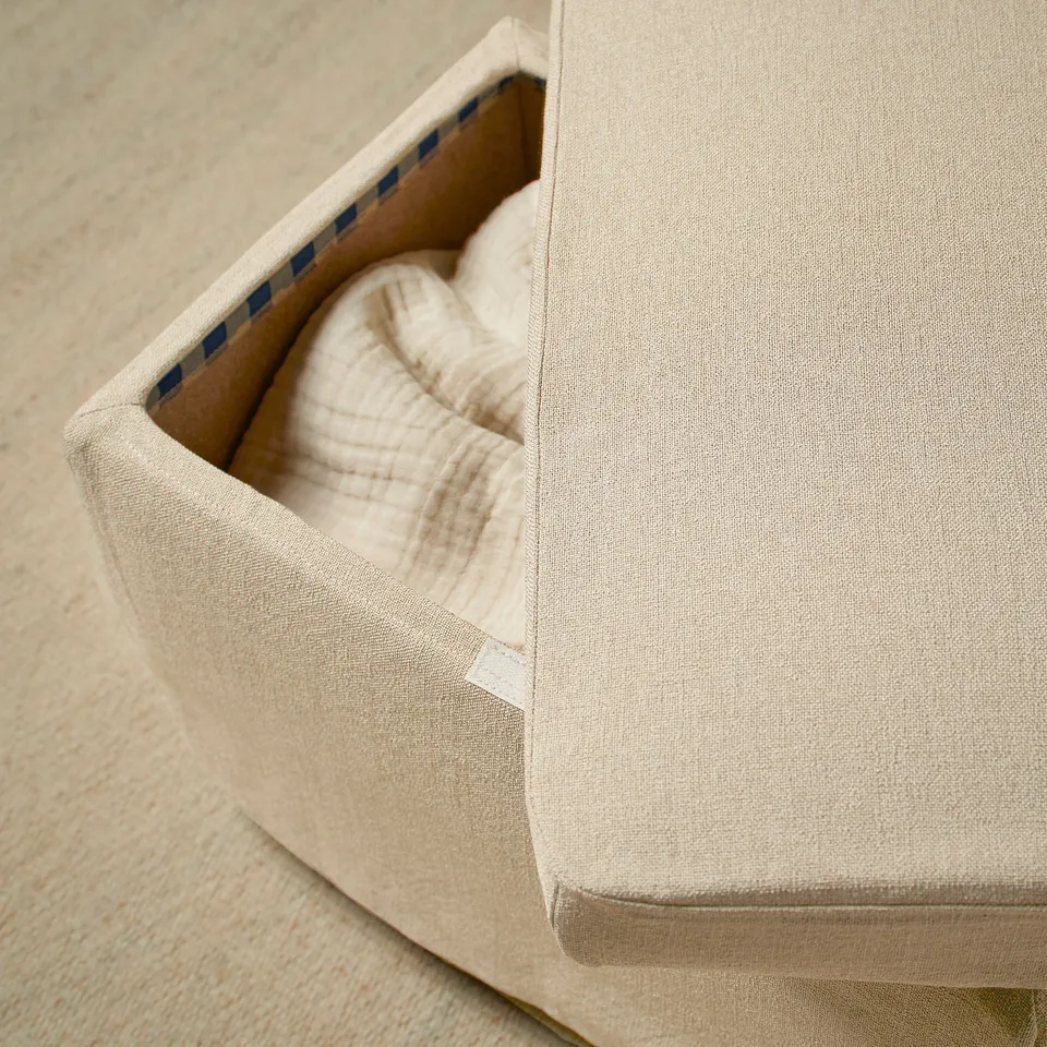 Neutral-colored fabric footstool with a beige muslin cloth resting inside, showcasing protective and stylish cover design.