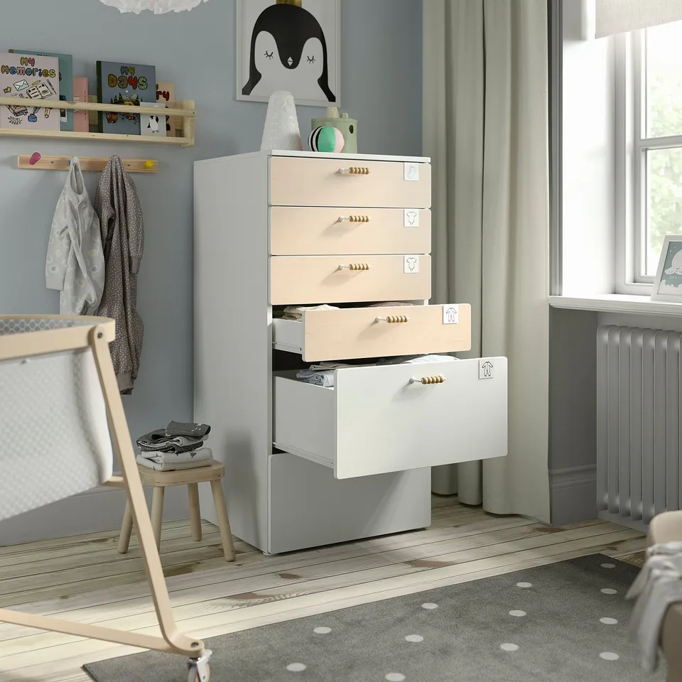 Toddler room with pastel drawers, open drawer, bookshelf, penguin art, stool, natural light.