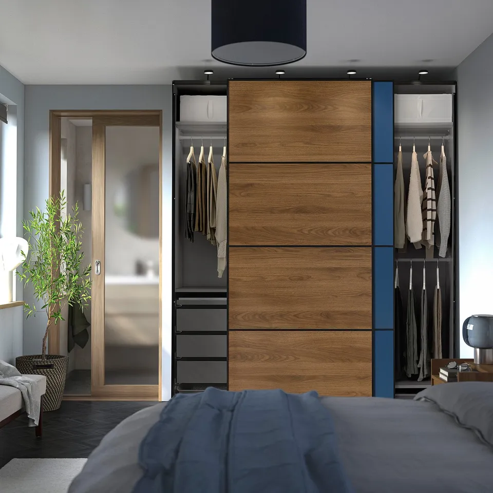 Bedroom with sliding door wardrobe. Wardrobe has hanging clothes, drawers, and wooden panels. Room includes bed, plant, and bedside table.