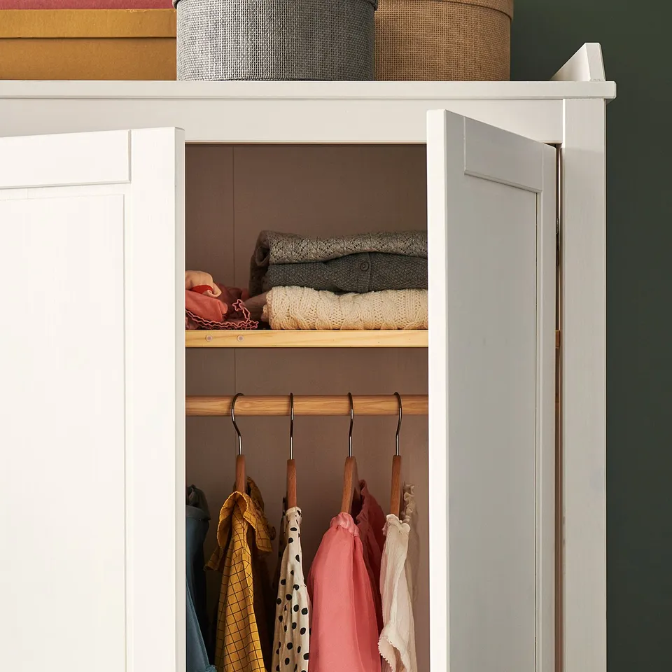 A well-organized closet with HÄNGA wooden hangers holding colourful childrens clothes. Bright garments hang neatly in a white wardrobe.