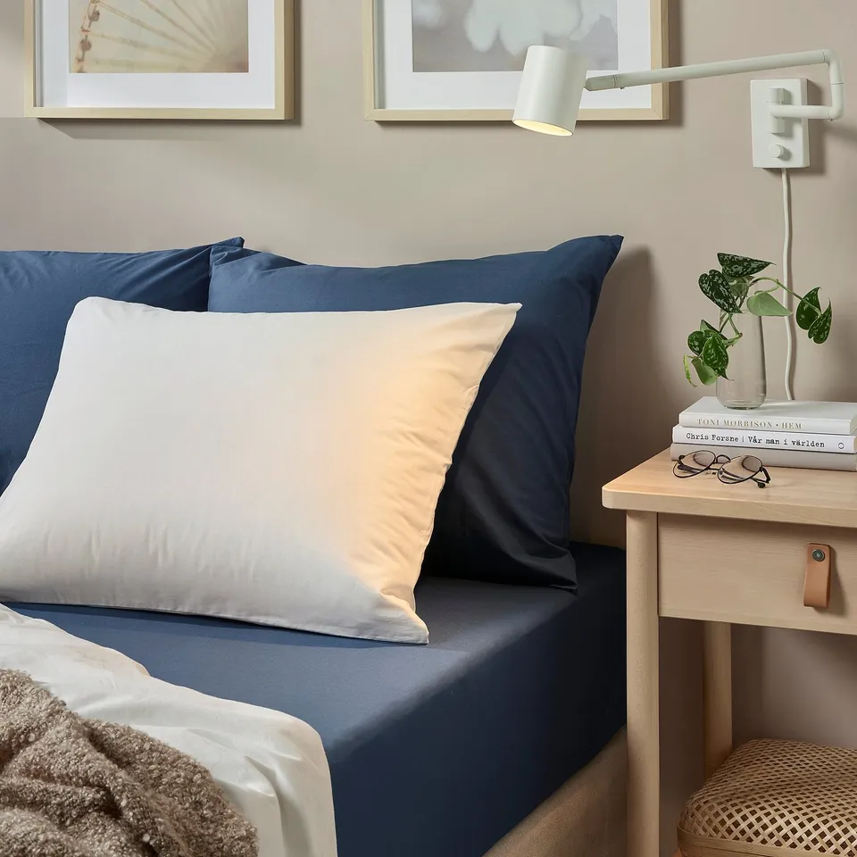 Bed with ULLVIDE blue sheets, beige pillows, wooden bedside table, plant, books, lamp.