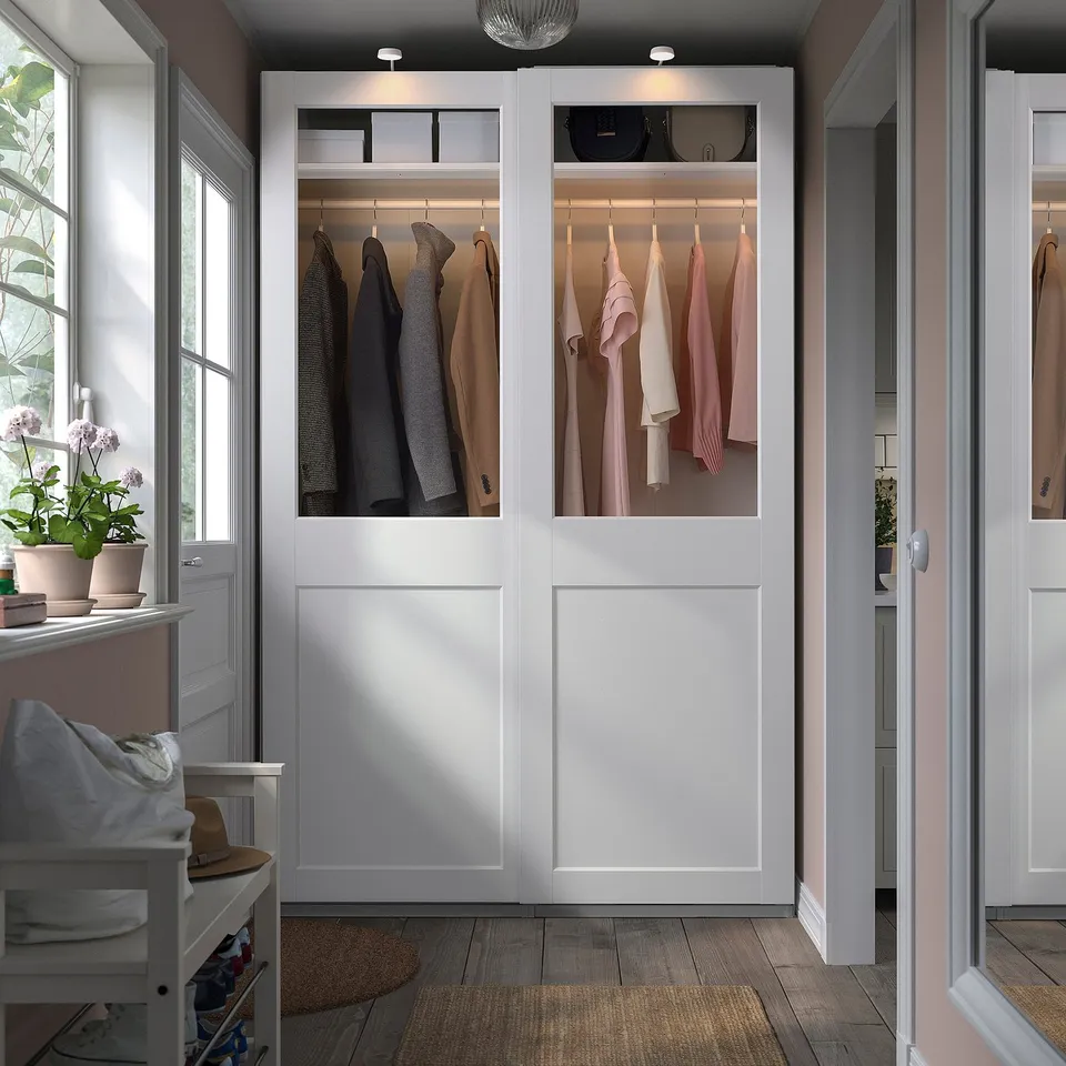 White PAX wardrobe with glass doors, clothes, and plants.