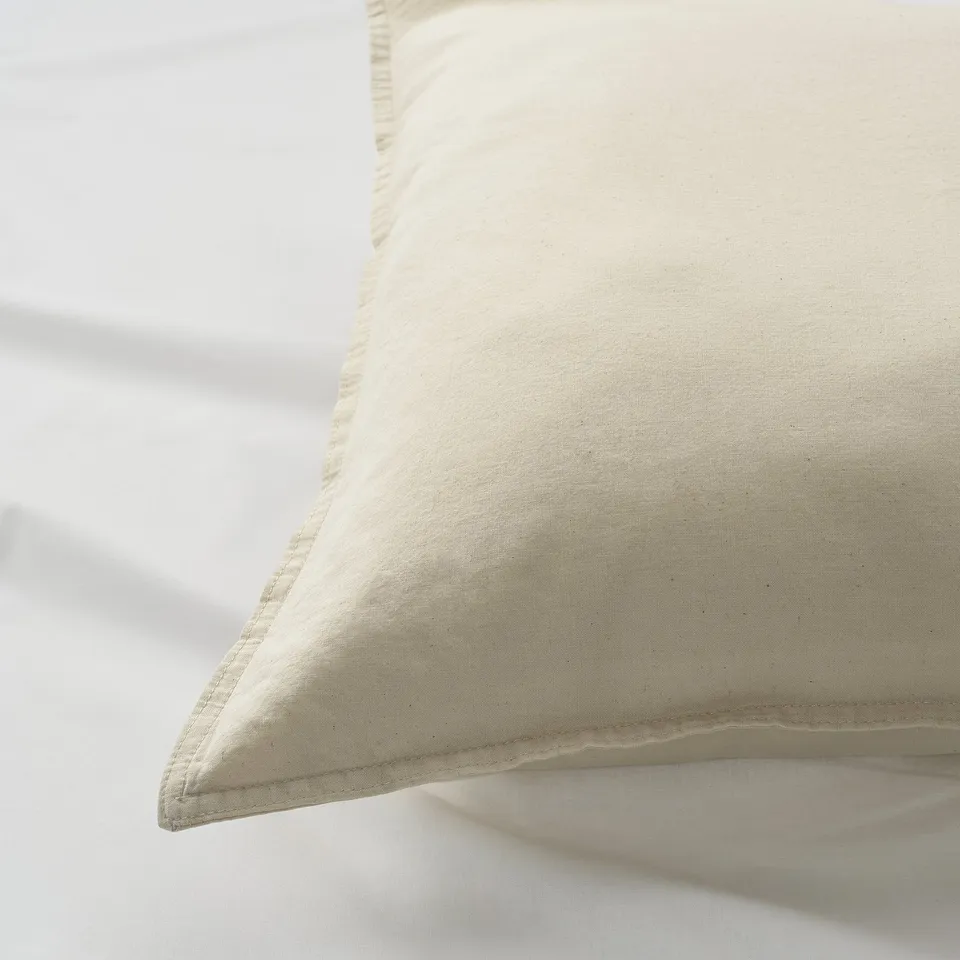 Close-up of a soft, creamy pillowcase with stitched edge detail, showcasing its smooth cotton texture and quality.