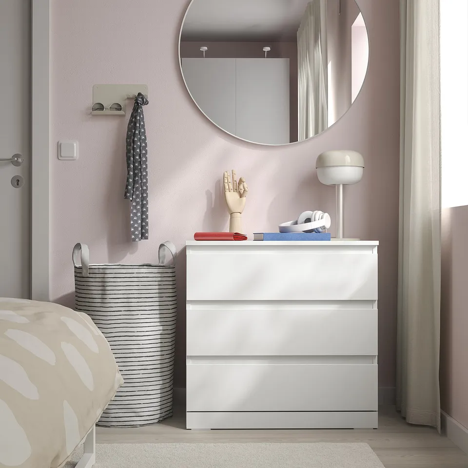 Small white LILLBERGET chest sits neatly by the bed, with rounded mirror above, stylish decor, and striped laundry basket beside.