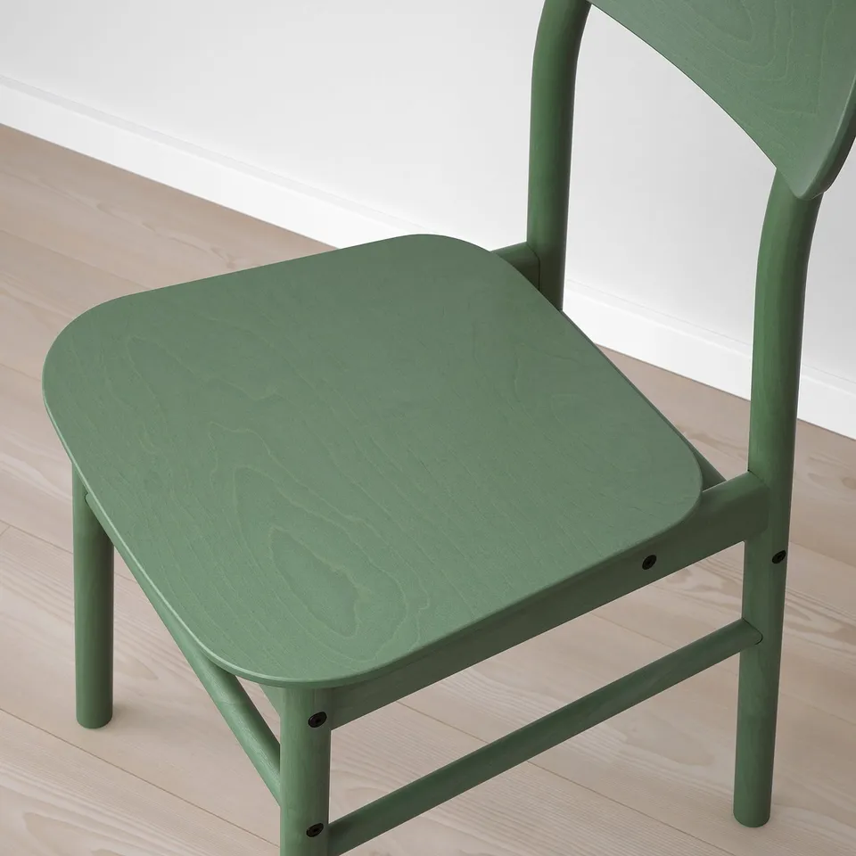 A pair of green wooden chairs with visible grain texture and smooth seats, placed on a light wooden floor.
