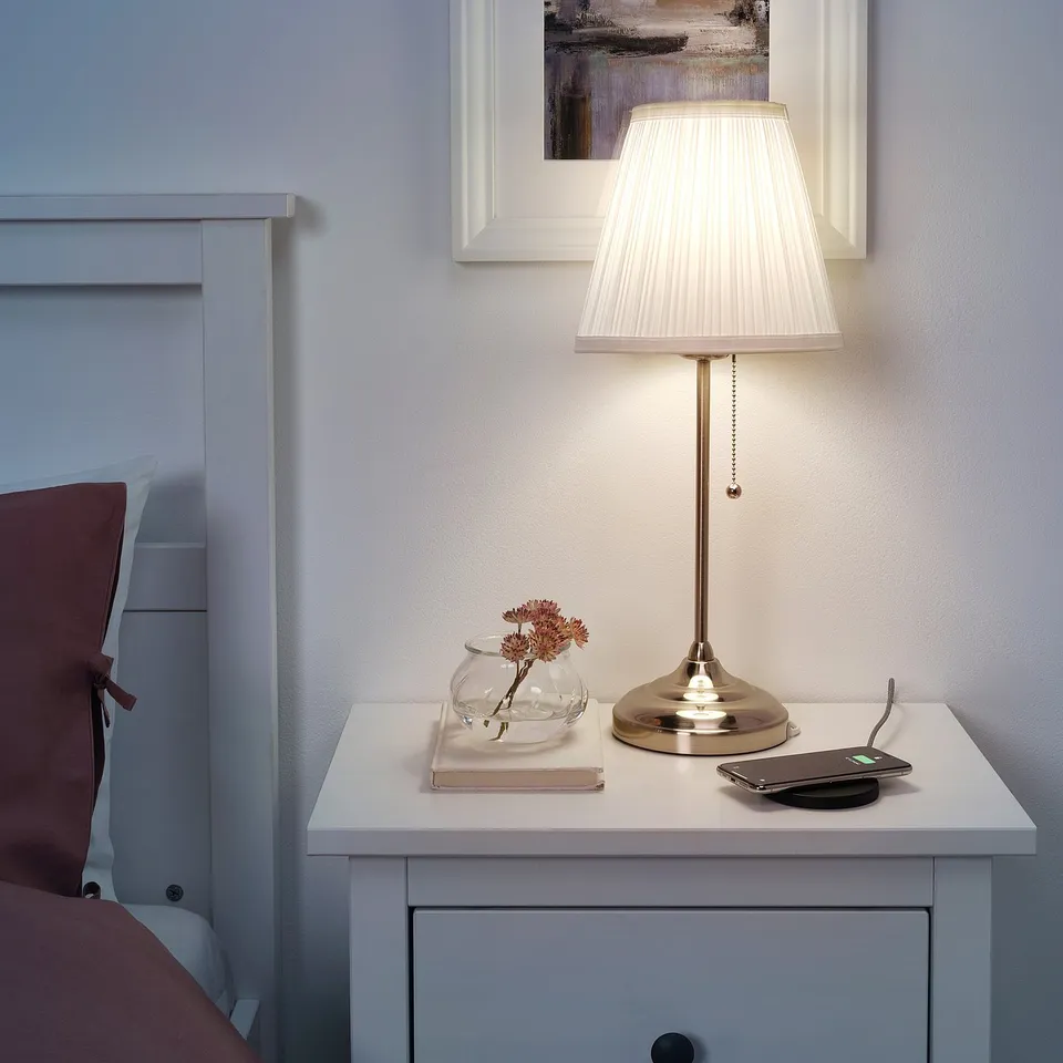 Ensed bedside table with white lamp, small vase, book, and phone. Clean, minimalist design.