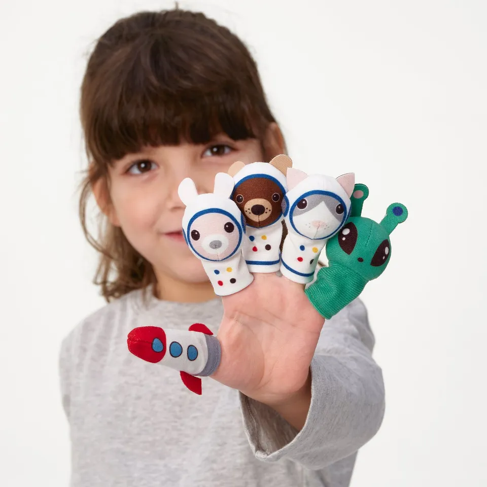 A young girl holding up five finger puppets in space-themed costumes.