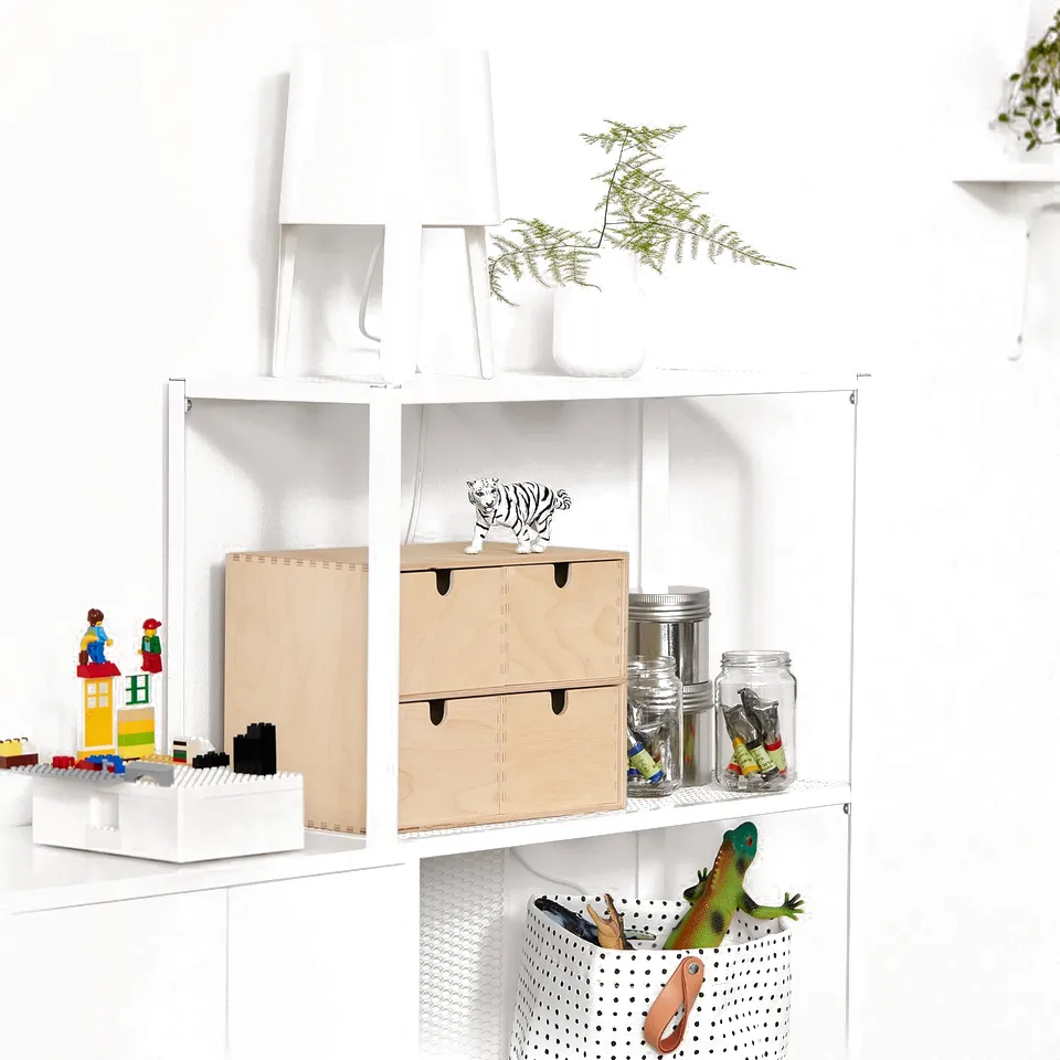 White metal storage shelf with wooden drawers, toy blocks, colourful toys, and a lamp. Modern, clean design.