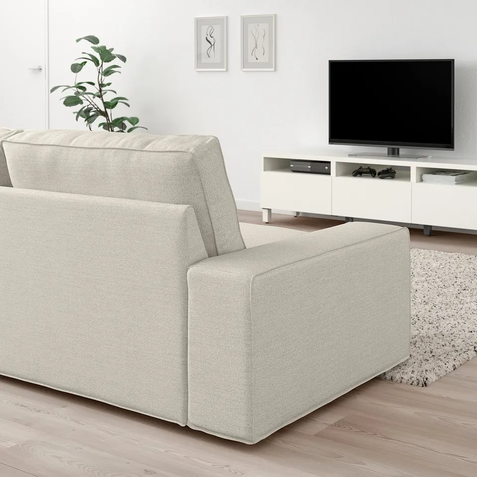 Modern living room with large beige KIVIK sofa, white tv stand, flat screen tv, plant, and rug.