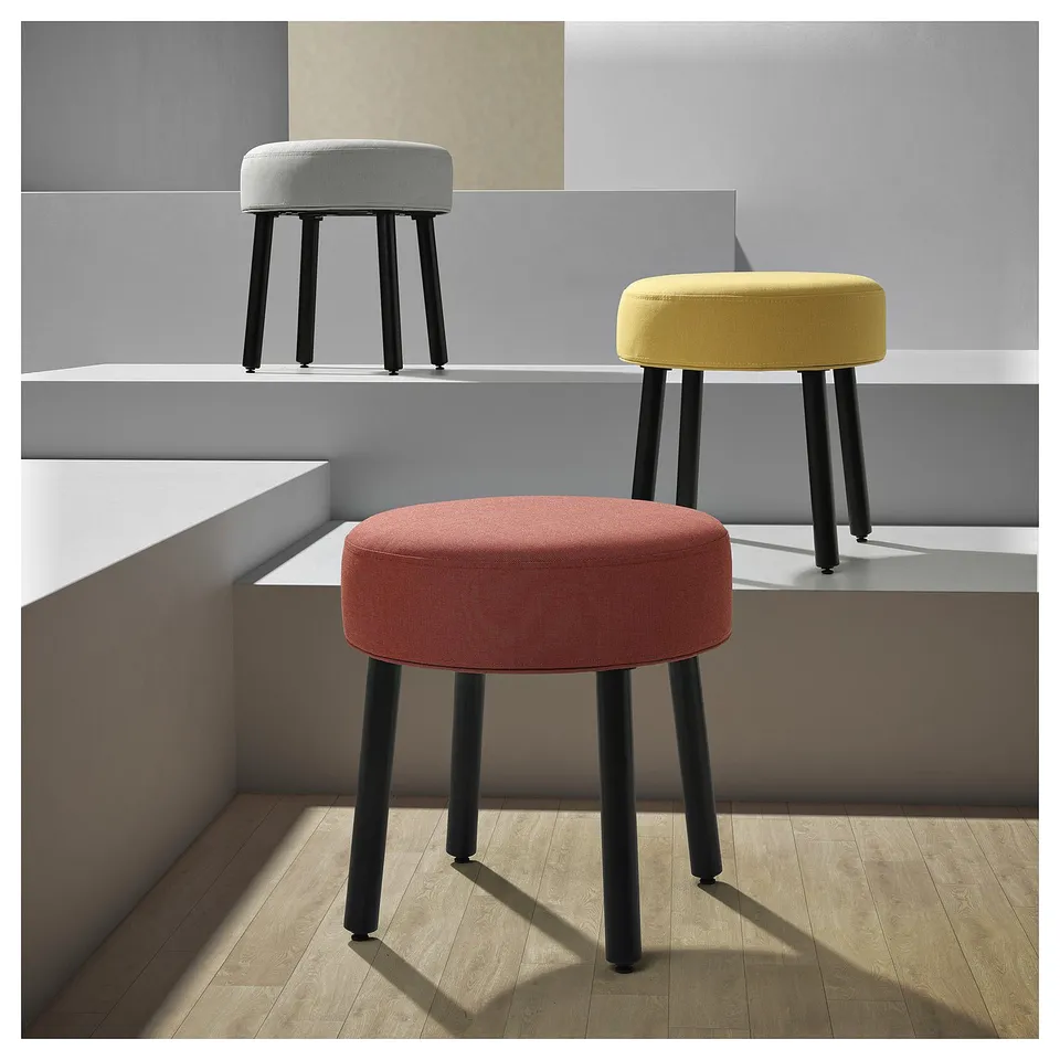 Three round, cushioned stools in red, yellow, and grey, with black metallic legs, stylishly placed in a modern room.