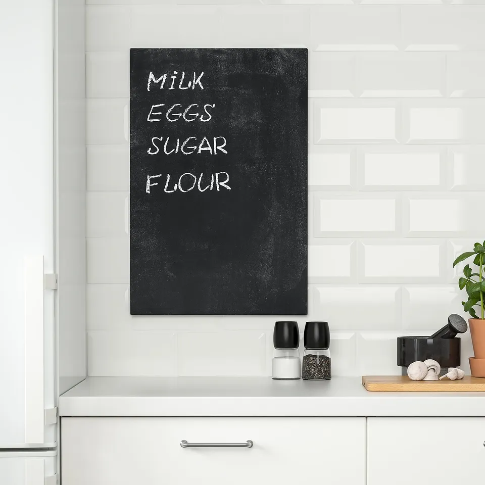 Black chalkboard on white wall for kitchen reminders, with salt, pepper, and plant below.