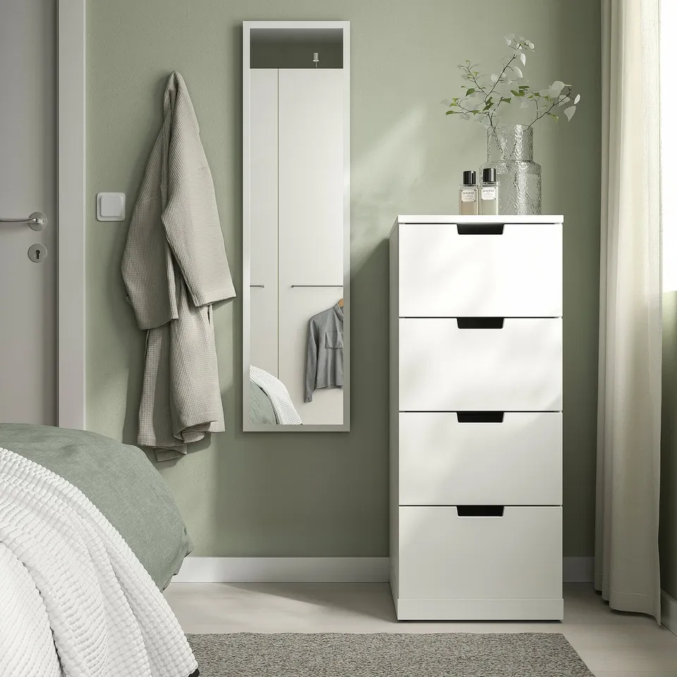 Modern bedroom with LILJETRÄD mirror & storage. White mirror with slim frame, dresser, vase, and robe. Calm, minimalist decor.
