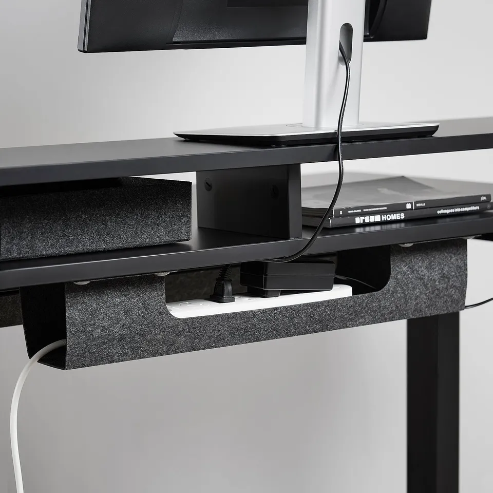 Black sit-stand desk with under-desk cable management compartment, showcasing organised wiring and a document shelf.