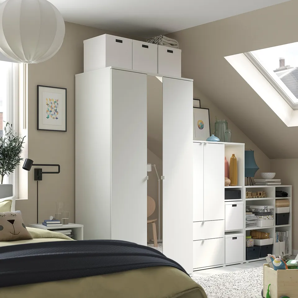 Modern white wardrobe with mirror and shelves, green bedding, wall lamp, and decorative items.