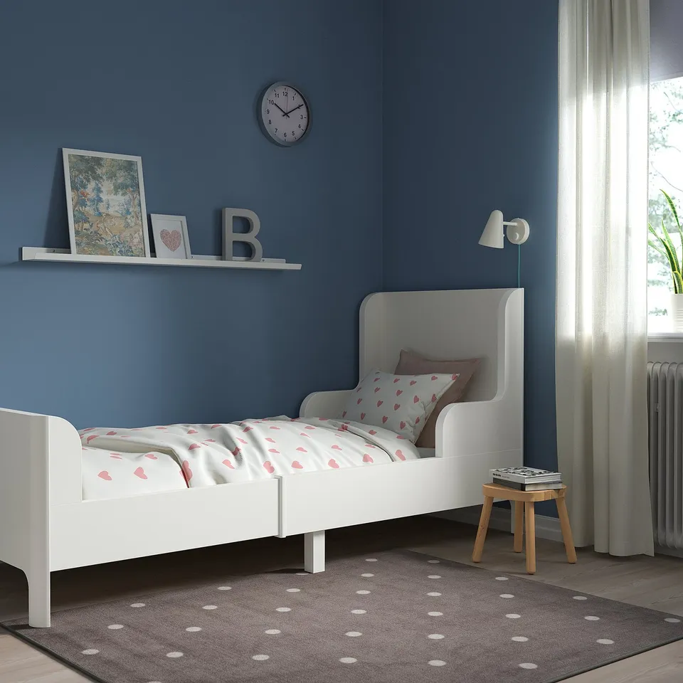 Blue kids bedroom with BUSUNGE white extendable bed. Bed rounded corners & matching bedding. Bright wall clock & natural light enhance cosy ambiance.