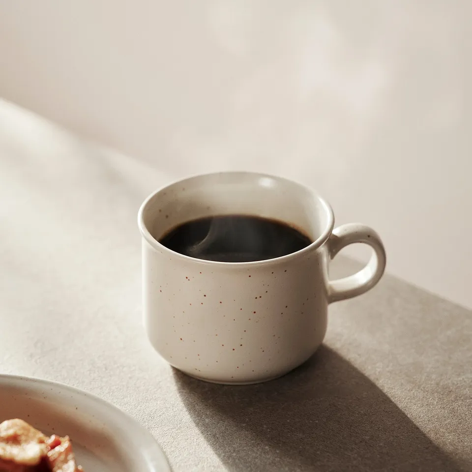 Small speckled mug of coffee on light fabric. Stoneware DAGGASTER set, rustic charm.