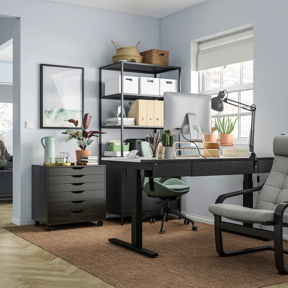 Modern home office with black TROTTEN desk, green chair, computer, plants, and grey walls.