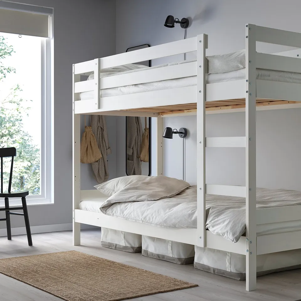 Wooden MYDAL bunk bed in white under window, with ladder, neutral linens, rug, wall lamps.