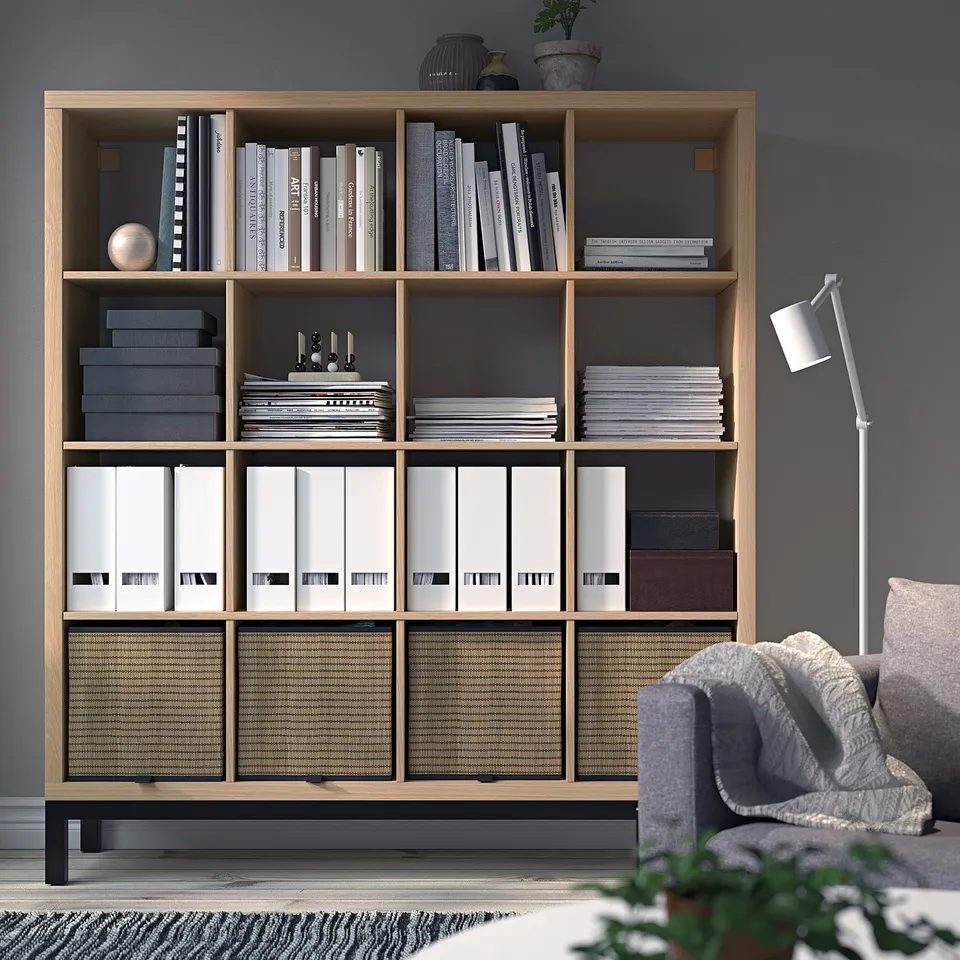 KALLAX oak shelving unit filled with books & binders, grey fabric chair, grey wall.