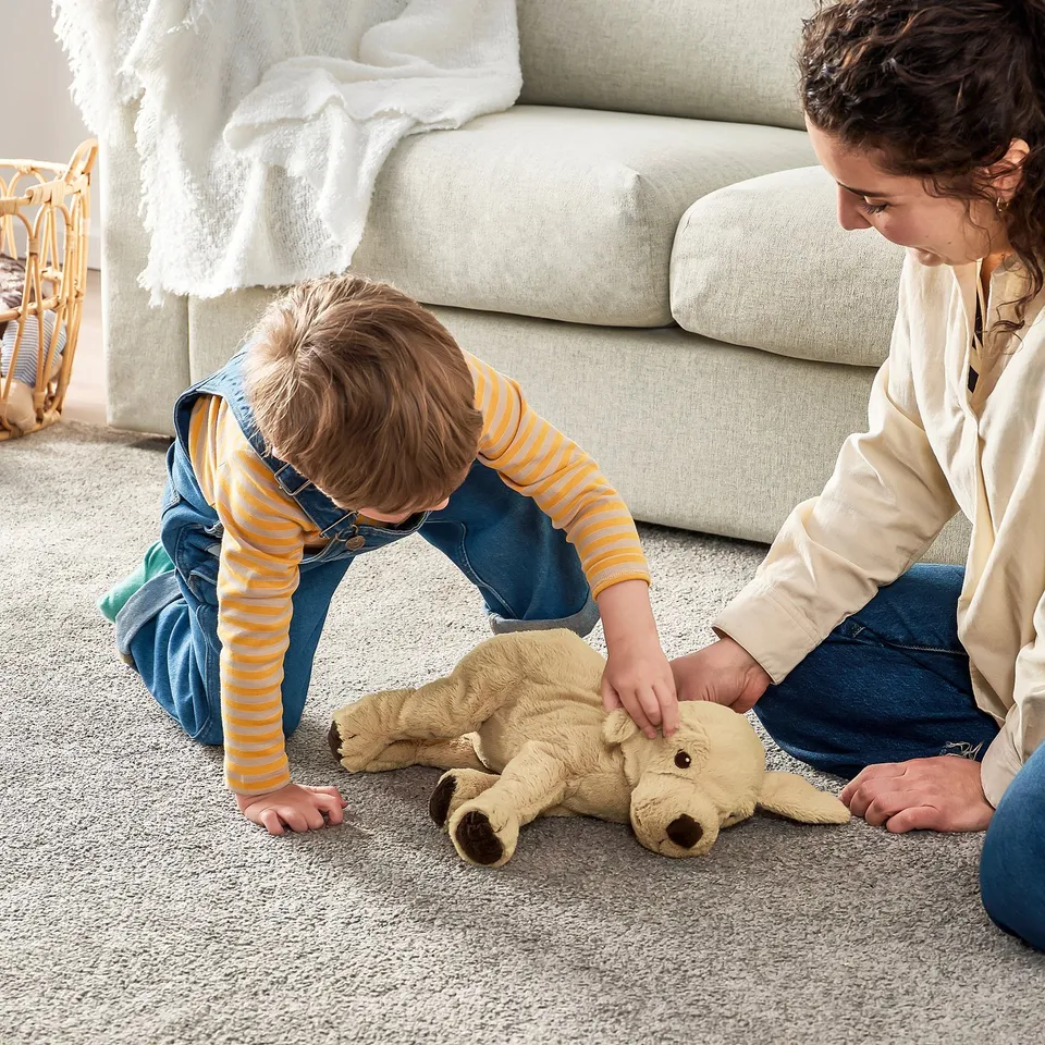 Two kids playing with soft toy on carpet near sofa.