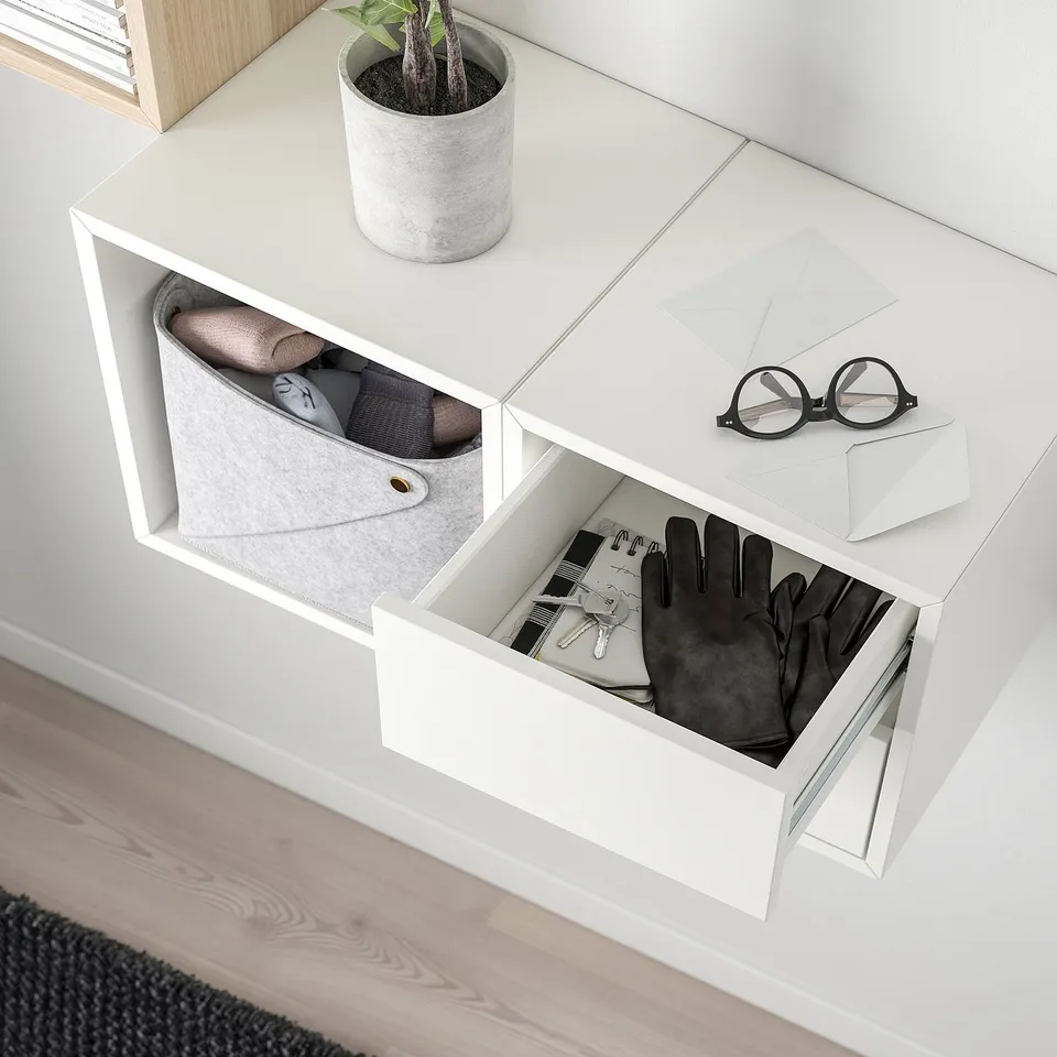 Wall-mounted storage with open shelves and drawers, showing gloves and keys, socks, and a potted plant on top.