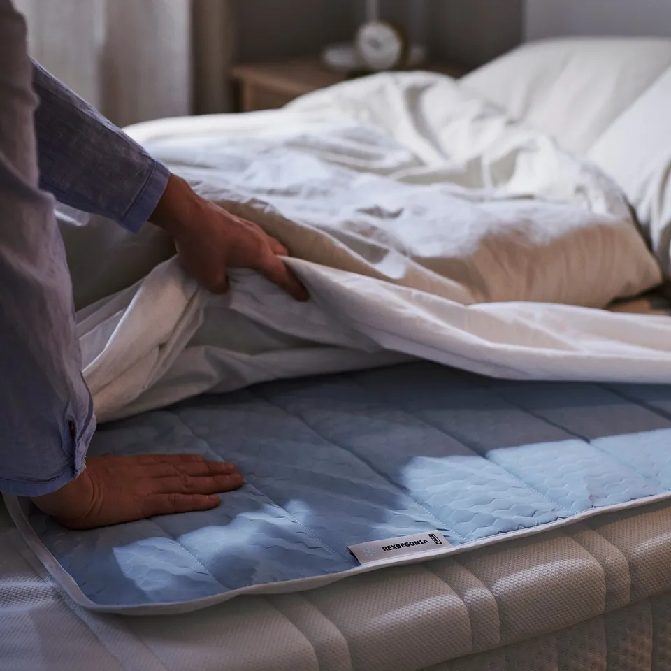 Person placing light blue REXBEGONIA cooling pad on bed.