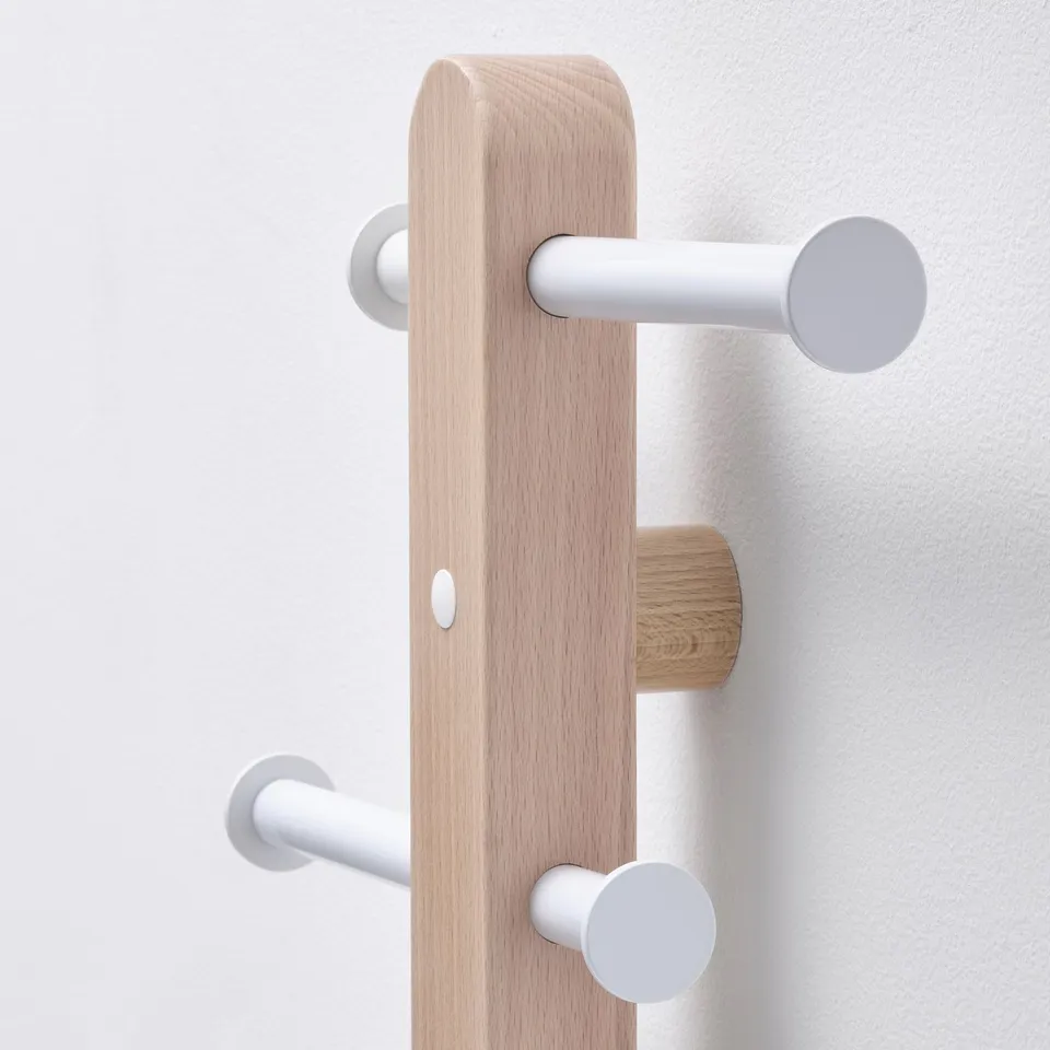 Minimalist wooden coat rack with three hooks, two white, one natural, mounted on a light wall.