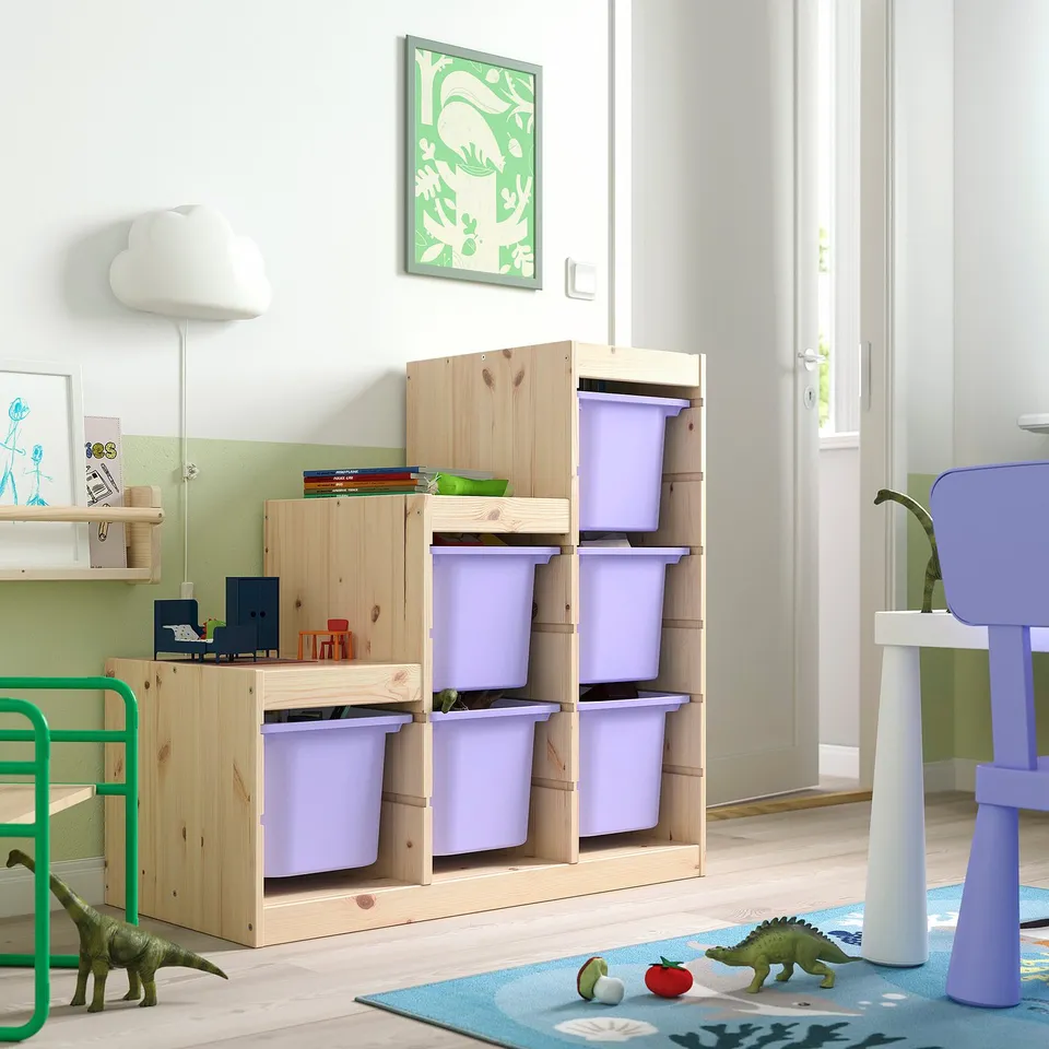 Childs room with wooden TROFAST storage, purple plastic bins, green toy dinosaurs, lamp, and artwork. Bins are stacked, with one below a small table.