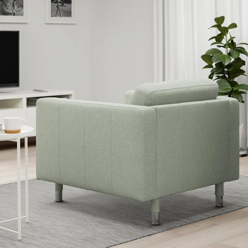 Light green armchair in modern room, beside small table with cup. Soft cushions and tight fit cover for comfort.