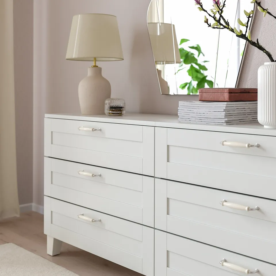 White drawer unit, modern design, six drawers with porcelain handles. Top holds lamp and decor items, stylish storage.