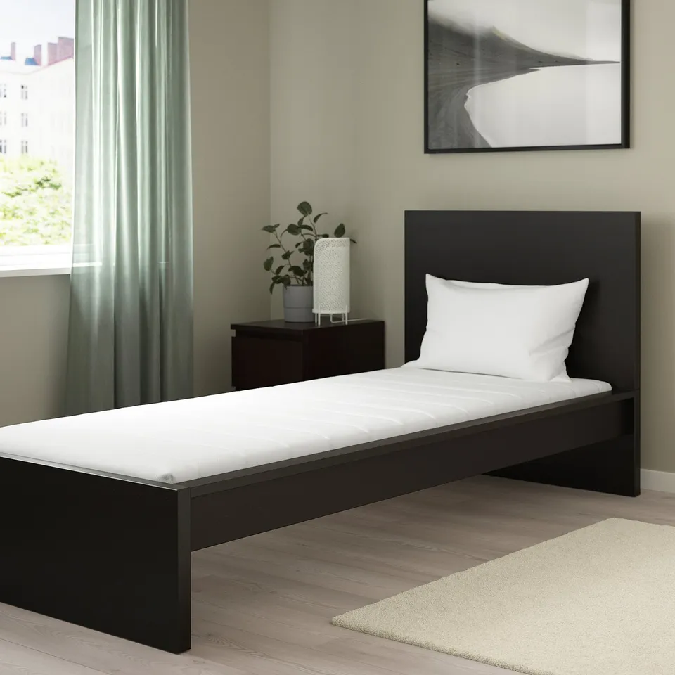 Black foam mattress in minimalist room, firm with washable cover, against wall.