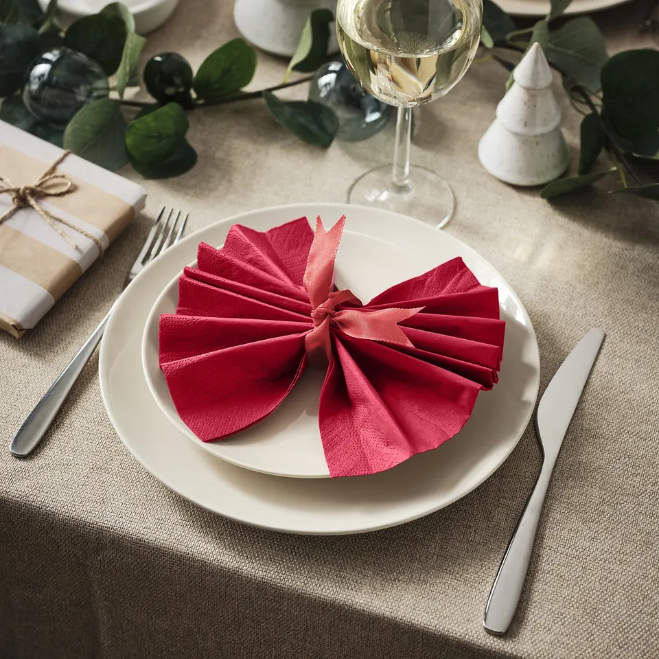 White plate with red folded napkin, knife, fork, and wine glass, decorative greenery