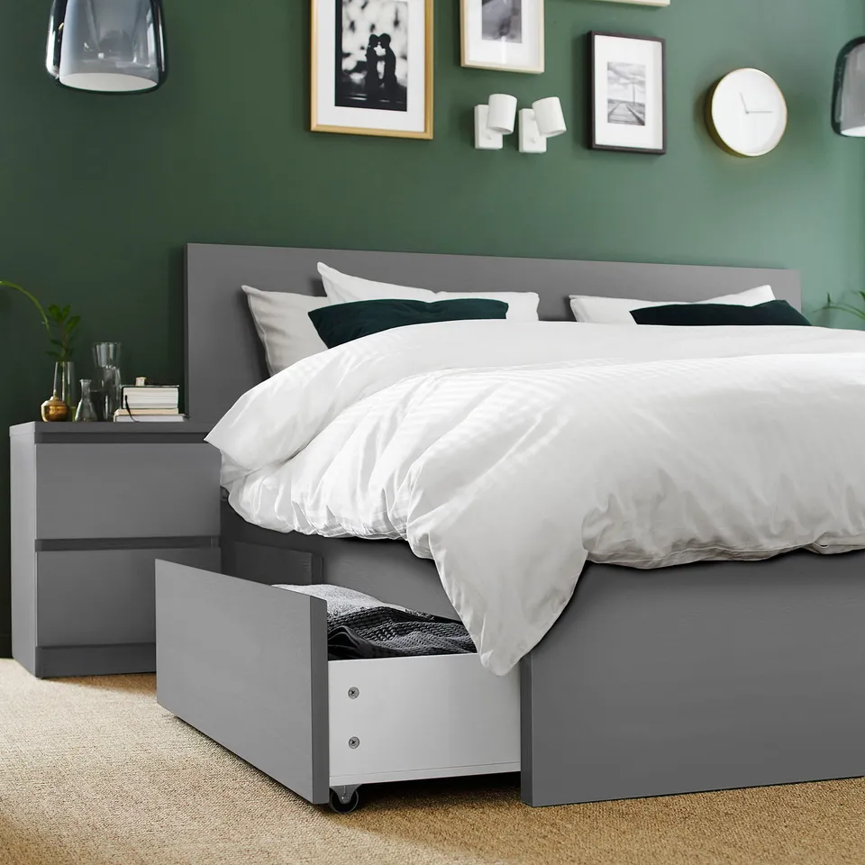 Modern grey bed with white linens, wooden bedside table, green wall, and artwork.