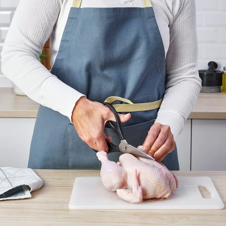 Person uses scissors to prepare chicken on cutting board in kitchen.