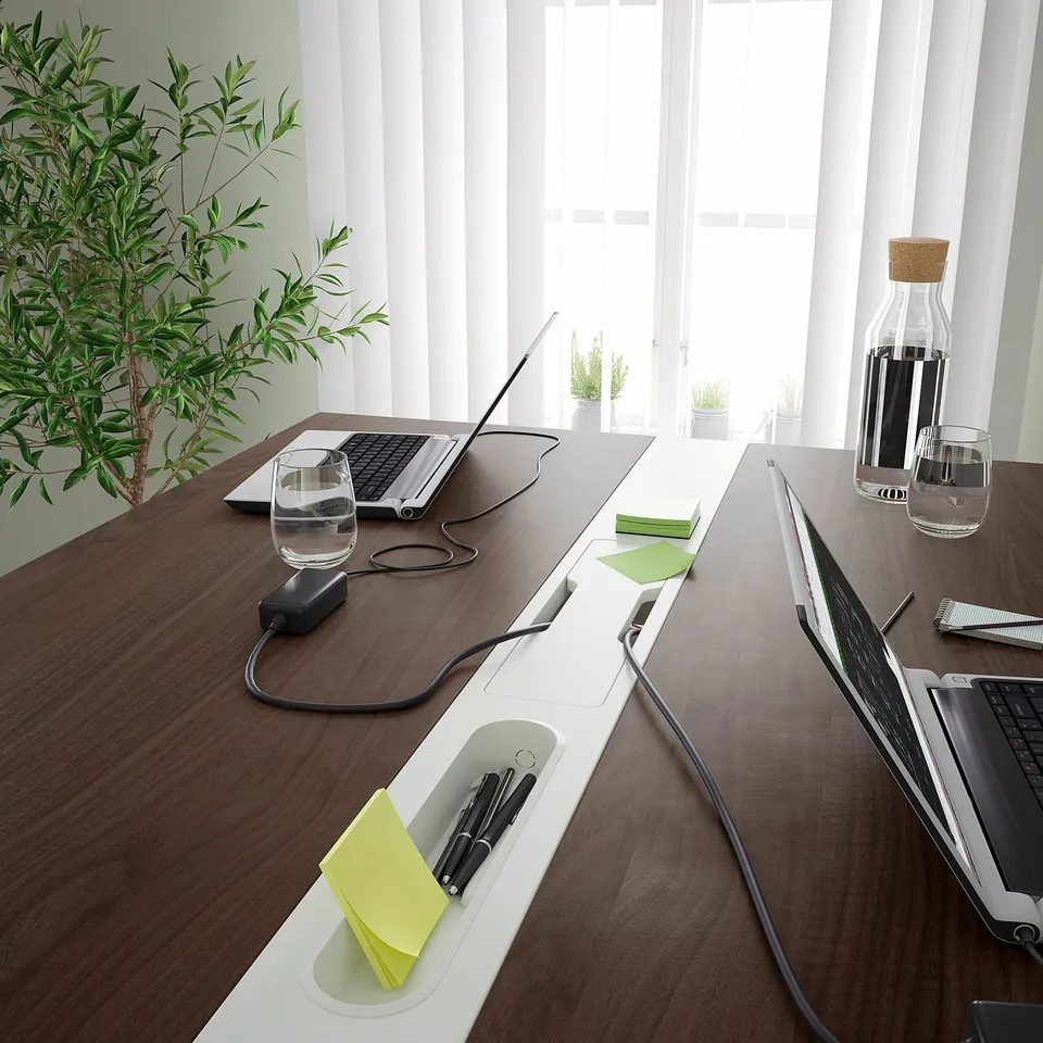 A modern conference table with integrated footrests and cable management, supporting both sitting and standing.