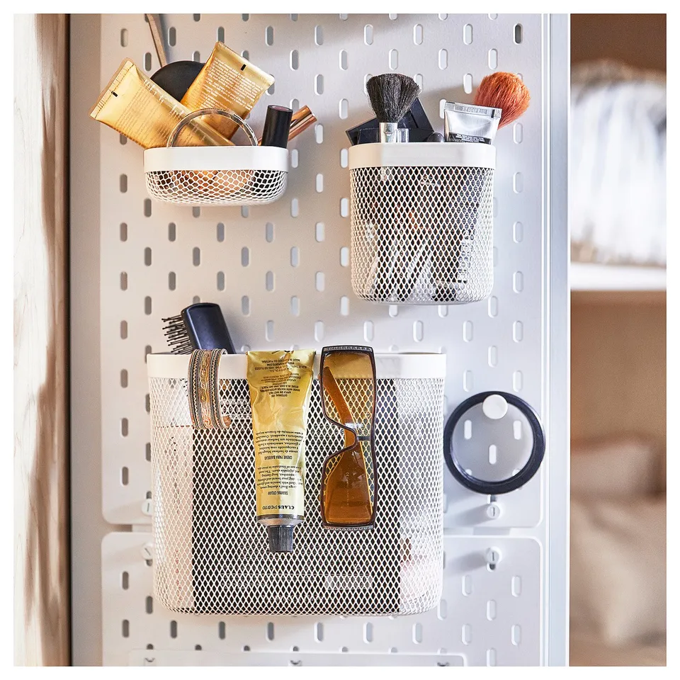 SKÅDIS white mesh organisers hang on pegboard; holds cosmetics, brushes, and tubes.