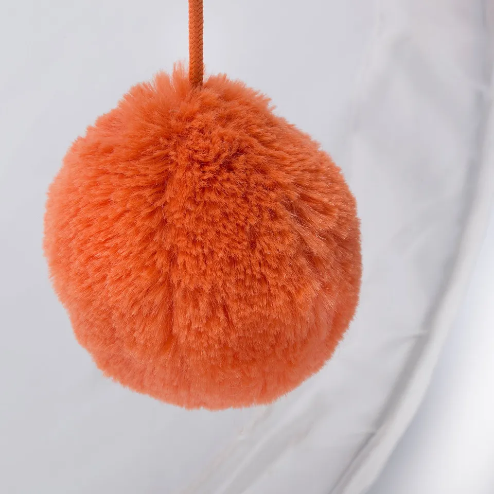 Large, fluffy orange pom-pom hanging, soft and plush texture.