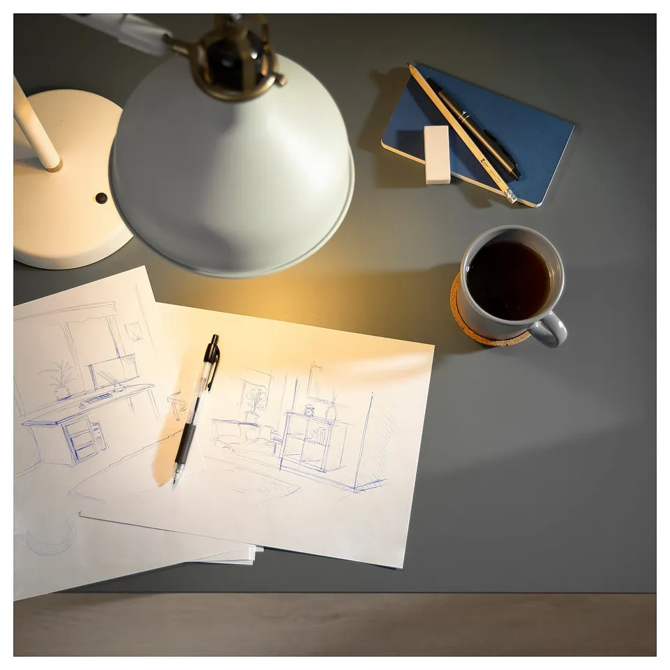 Desk setup with LAGKAPTEN table, lamp, notebook, coffee, and blueprint sketch.