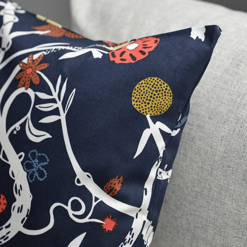 Decorative pillow with intricate floral pattern in various colours on dark background, sitting on light-colored sofa. Zip closure.