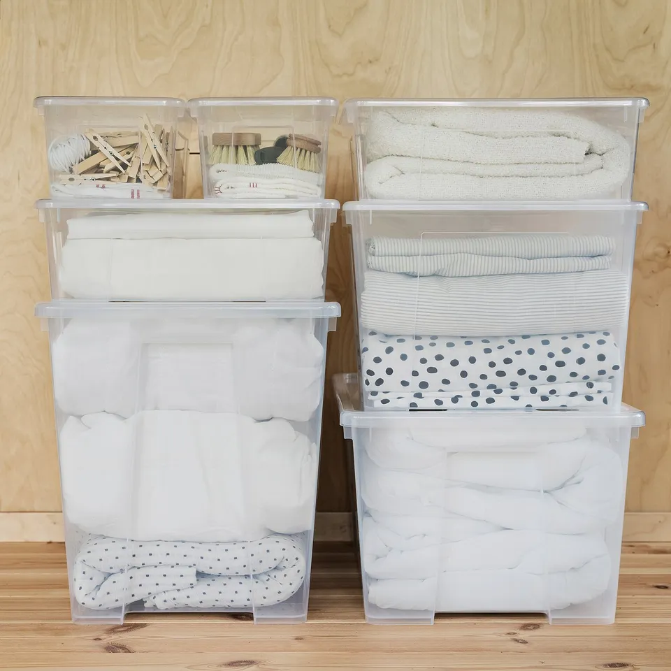 Four stacked SAMLA boxes with folded clothes. Top two small, middle medium, bottom large. Transparent, contents visible.