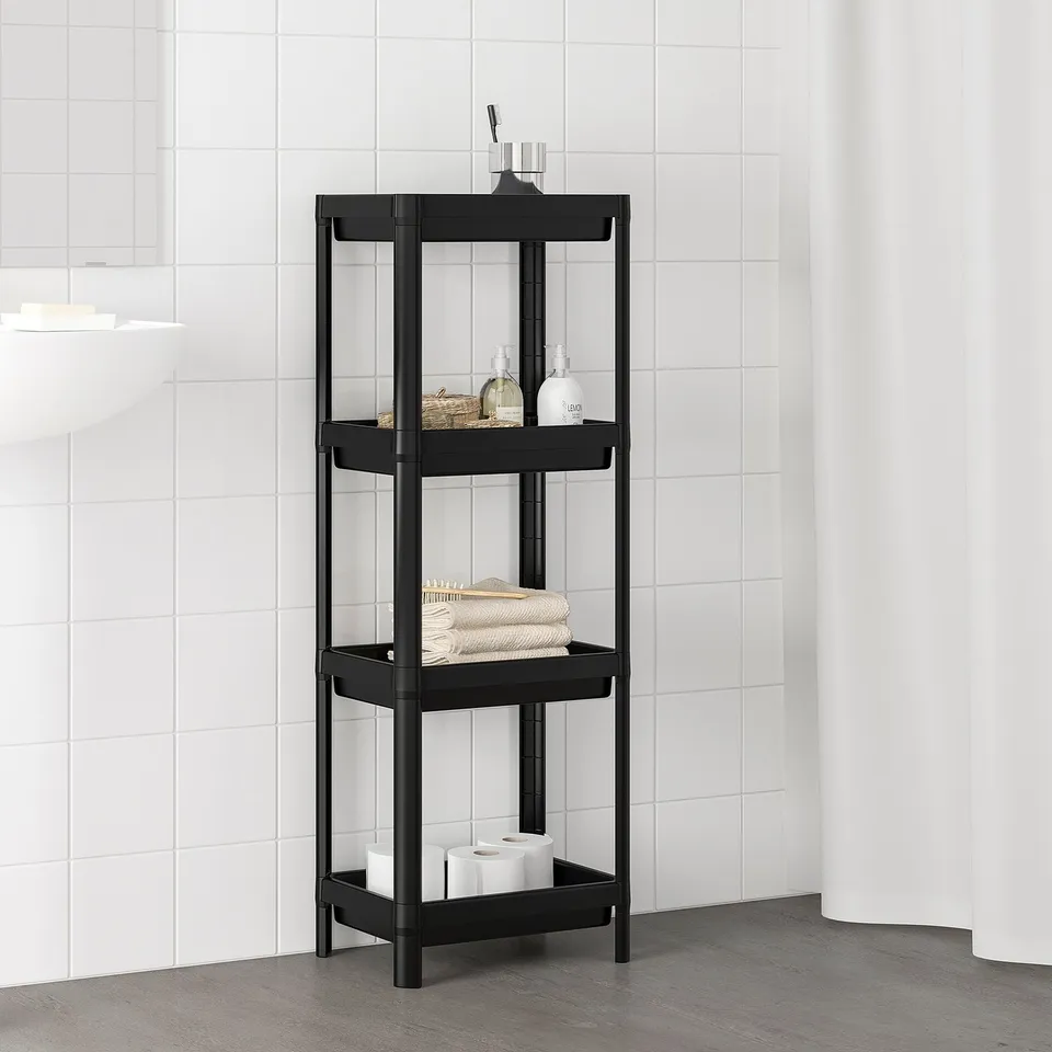 Black VESKEN 4-tier bathroom organiser. Slim, rectangular, modern. Holds toiletries between white-tiled walls.
