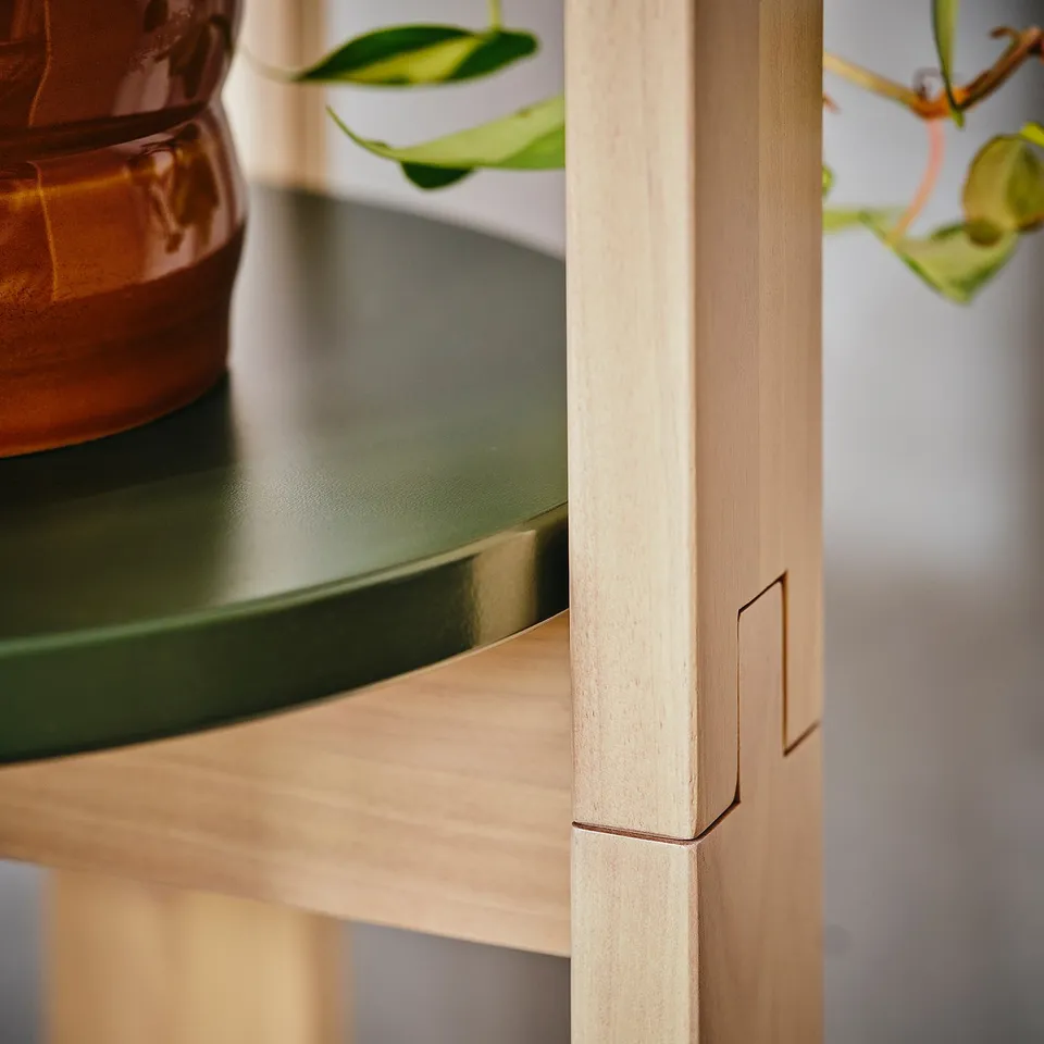 Close-up of wooden stool leg with groove detail. Top shelf visible, holding a terracotta pot with plant.